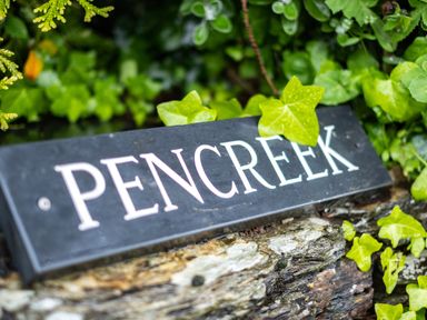 A black sign with the word Pencreek surrounded by green leaves and placed on a stone surface at Pencreek in Rock