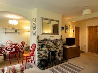 A living room with a stone fireplace and a dining area with red chairs at Pencreek in Rock