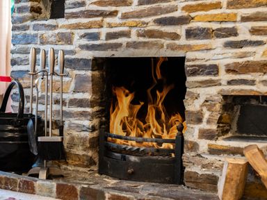 A stone fireplace with a burning fire and fireplace tools at Pencreek in Rock