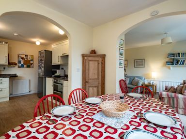 A dining table with plates and cutlery and red chairs between a kitchen and a living room at Pencreek in Rock