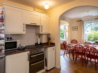 A kitchen with white cabinets and a microwave next to a dining area with a table covered by a red and white patterned tablecloth and red chairs at Pencreek in Rock
