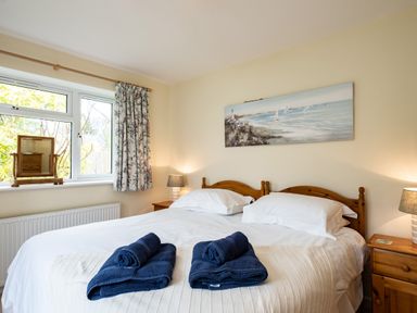 A bedroom with a double bed with white linen and blue towels on top two bedside tables with lamps and a window with floral curtains at Pencreek in Rock