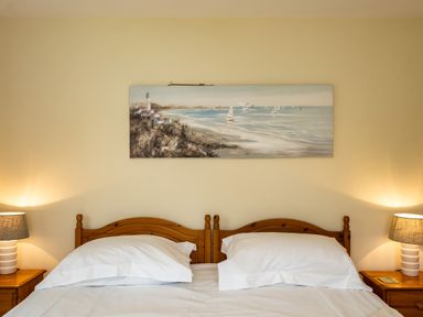 A bedroom with two beds side by side wooden headboards two bedside tables with lamps and a coastal painting on the wall at Pencreek in Rock