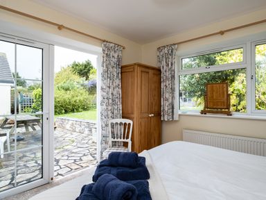 A bedroom with a bed and folded towels next to a wooden wardrobe and a chair by the door leading to a garden at Pencreek in Rock