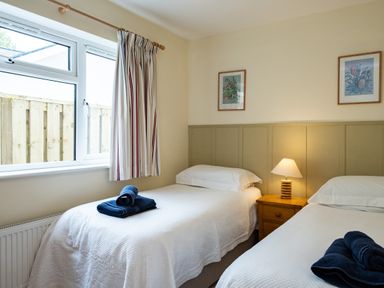 A bedroom with two single beds with white covers and blue towels a wooden nightstand with a lamp and framed pictures on the wall at Pencreek in Rock