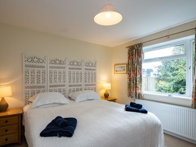 A bedroom with a large bed two bedside tables with lamps and a window with floral curtains at Pencreek in Rock