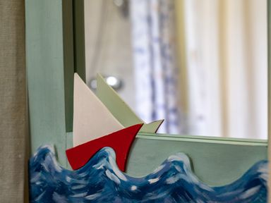 A close-up of a mirror frame with a painted blue wave design and a small red and white sailboat at Pencreek in Rock