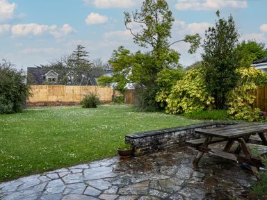 A garden with grass trees a stone patio and a wooden picnic table at Pencreek in Rock
