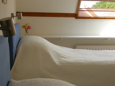 A bedroom with two beds covered in white patterned bedspreads and a window with a wooden frame at Rosevallen in Daymer Bay