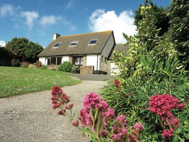 A detached house with a sloped roof and skylights with a garden and a driveway with flowers at Rosevallen in Daymer Bay