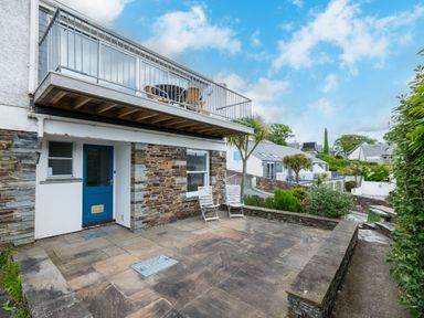 Exterior view of a house with blue door stone walls a patio with two chairs and a balcony above at Slipway 7 Rock