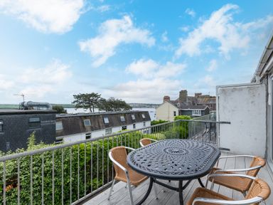 A balcony with a metal table and four chairs overlooking rooftops and water at Slipway 7 in Rock
