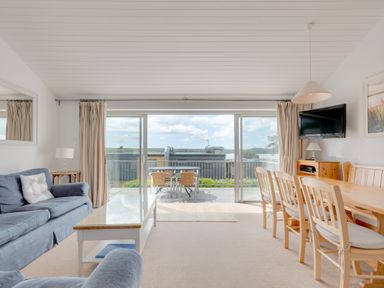 A living room with blue sofas a wooden dining table with chairs and a glass coffee table with sliding doors leading to an outdoor seating area at Slipway 7 in Rock