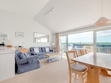 A living area with blue sofas a wooden dining table and chairs and large glass sliding doors with a view at Slipway 7 in Rock