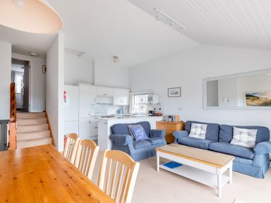 A living area with blue sofas a wooden dining table white kitchen cabinets and a staircase at Slipway 7 in Rock