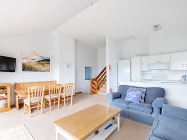 An open living area with a dining table and chairs a blue sofa and armchair a wooden coffee table and a kitchen in the background at Slipway 7 Rock