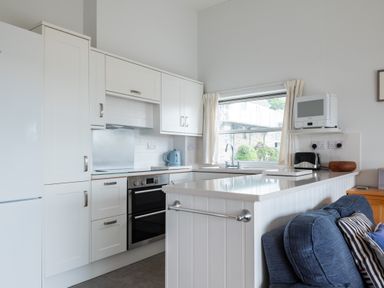 A kitchen with white cabinets a double oven a refrigerator a microwave toaster kettle and a blue sofa at Slipway 7 in Rock