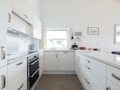 A kitchen with white cabinets a double oven a window above a sink and countertop items at Slipway 7 in Rock