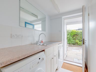 A utility room with a washing machine sink dishwasher and door leading outside at Slipway 7 in Rock