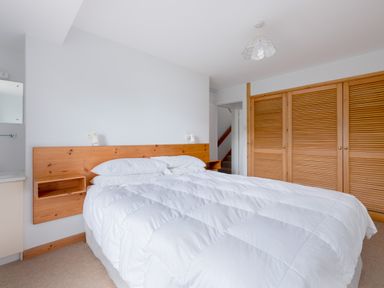 A bedroom with a large bed with white bedding a wooden headboard built-in shelves wooden wardrobes and a door leading to a stairway at Slipway 7 in Rock