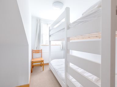 A small bedroom with a white bunk bed and a wooden chair by a window at Slipway 7 in Rock