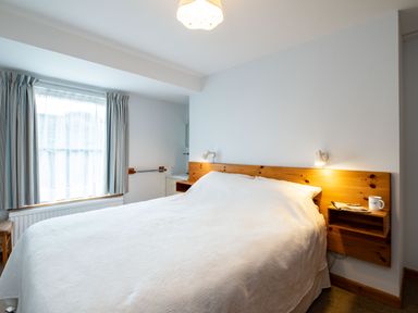 A bedroom with a large bed white bedding wooden headboard reading lights window with curtains and a mug on a shelf at Slipway 7 in Rock
