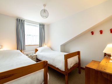 A bedroom with two single wooden beds a window with curtains a nightstand a desk with a lamp and coat hooks on the wall at Slipway 7 Rock