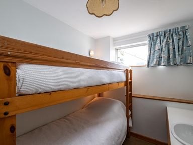 A small bedroom with wooden bunk beds and a window with blue patterned curtains at Slipway 7 in Rock