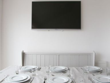 A dining table set with plates glasses and cutlery below a wall mounted television at Slipway 10 in Rock