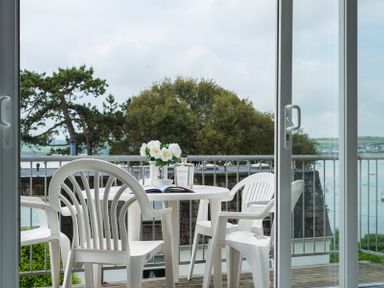 A balcony with a white plastic table and chairs with flowers on the table overlooking trees and water at Slipway 10 in Rock