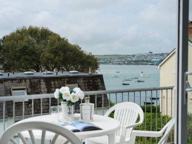 A balcony with white plastic chairs and a table with flowers a book and a glass overlooking boats on water at Slipway 10 in Rock