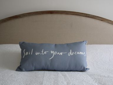 A pillow with text sail into your dreams on a white bed with a beige headboard at Slipway 10 in Rock