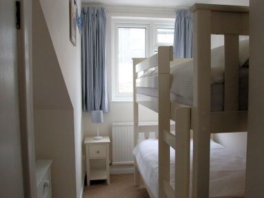 A bedroom with bunk beds, bedside table with lamp, window with curtains at Slipway 10 in Rock