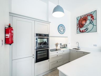 A kitchen with white cabinets built in oven stove sink clock and crab painting at Slipway 10 in Rock