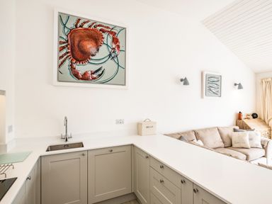 A kitchen area with light gray cabinets and a white countertop next to a beige sofa with decorative pillows at Slipway 10 in Rock