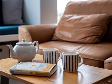 A wooden table with a white teapot two striped mugs and a book in front of a brown leather sofa at Slipway 15 in Rock