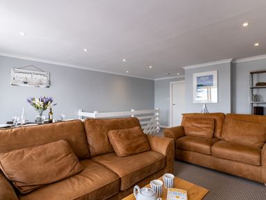 A living room with brown sofas a wooden coffee table with cups and teapot and a dining table with flowers at Slipway 15 in Rock