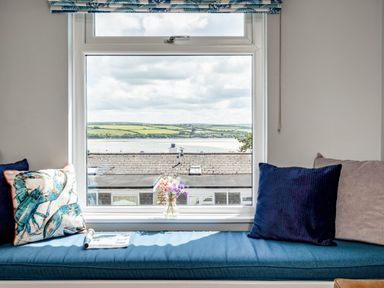 A window seat with cushions and a small flower vase overlooking rooftops and countryside at Slipway 15 in Rock