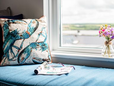 A window seat with a crab printed cushion a rolled magazine glasses and a vase with flowers at Slipway 15 in Rock