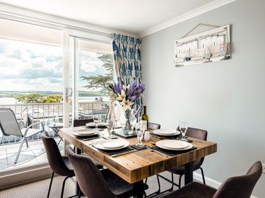 A dining area with a wooden table set with plates and glasses next to a sliding glass door with blue patterned curtains and a balcony at Slipway 15 in Rock