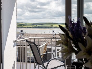 A balcony with a chair overlooking rooftops water and green hills at Slipway 15 in Rock