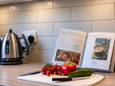 A kitchen counter with a kettle an open cookbook tomatoes a green pepper and a knife on a cutting board at Slipway 15 Rock