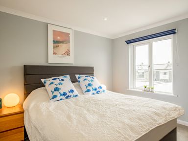 A bedroom with a bed two blue fish patterned pillows a side table with a round lamp a window and a framed artwork on the wall at Slipway 15 in Rock
