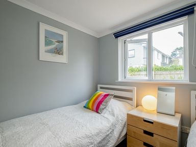 A bedroom with a single bed a bedside table with a lamp and mirror and a window with a blue blind at Slipway 15 in Rock