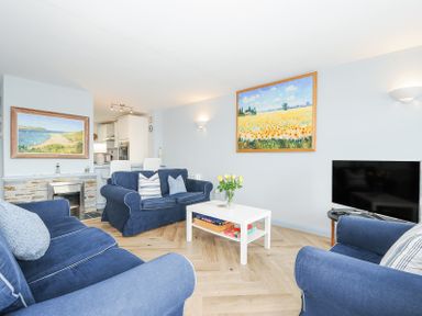 A living room with blue sofas a white coffee table with board games a TV and paintings on the walls at Slipway 16 in Rock