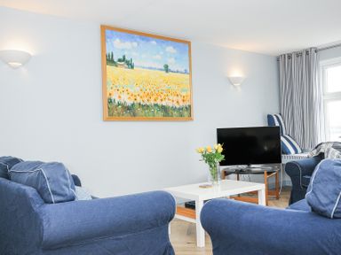 A living room with blue sofas a white coffee table a TV a painting of a field and flowers at Slipway 16 in Rock