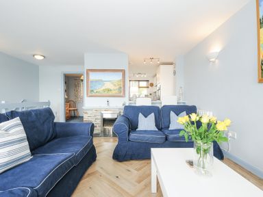 A living room with blue sofas a white coffee table with yellow flowers and a painting above a fireplace at Slipway 16 in Rock