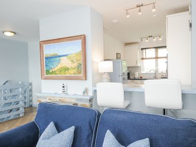 A living room with a blue sofa and pillows next to a kitchen with white chairs at Slipway 16 Rock