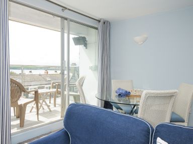 A living room with a glass dining table and white wicker chairs next to a sliding glass door leading to a balcony with plastic chairs and a table at Slipway 16 in Rock