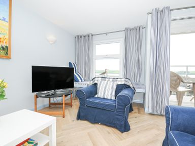 A living room with blue armchairs a TV on a wooden stand striped curtains and a window seat at Slipway 16 in Rock